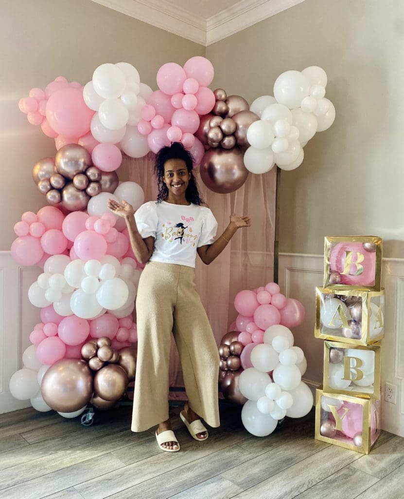 Picture of Bre in front of an organic balloon arch garland with photo backdrop and oversized blocks spelling BABY in a tower
